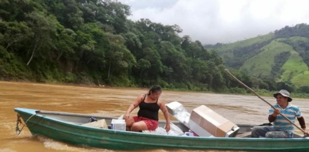 En un bote dos personas cruzan un río con los materiales donados.