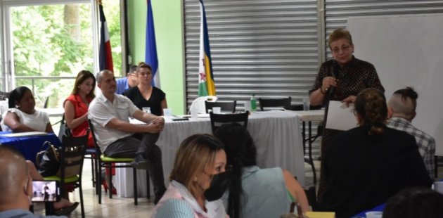 Personas escuchan palabras de la ministra, que está de pie al lado de una pizarr