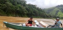 En un bote dos personas cruzan un río con los materiales donados.
