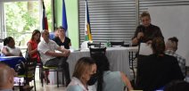 Personas escuchan palabras de la ministra, que está de pie al lado de una pizarr