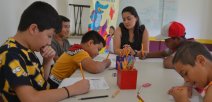 Niños y niñas escribiendo y coloreando, acompañados de una docente