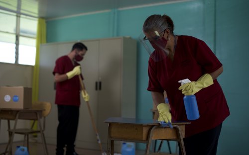 Fotografía de conserjes con mascarilla y guantes, desinfectando un aula