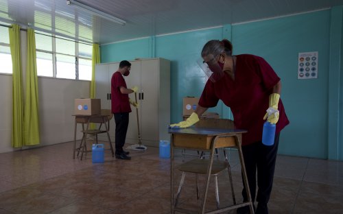 Fotografía de conserjes con mascarilla y guantes, desinfectando un aula