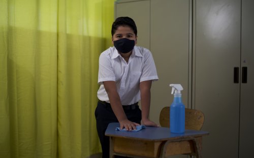 Estudiante limpiando un pupitre dentro de un aula
