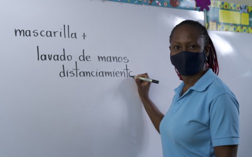 Docente con mascarilla escribiendo en una pizarra: mascarilla + lavado de manos 