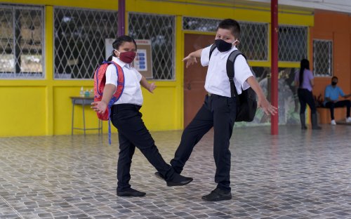 Dos estudiantes saludándose con el pie en el pasillo de un centro educativo