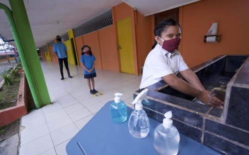 Tres estudiantes con mascarilla en el centro educativo haciendo fila