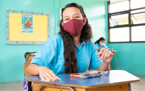 Estudiante con mascarilla en un aula, limpiando su pupitre
