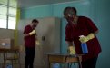 Fotografía de conserjes con mascarilla y guantes, desinfectando un aula