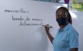 Docente con mascarilla escribiendo en una pizarra: mascarilla + lavado de manos 