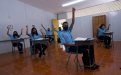 Varios estudiantes con mascarilla en un aula con las manos levantadas