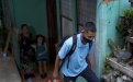 Estudiante con mascarilla saliendo de su casa, familia al fondo despidiéndose 