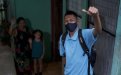 Estudiante con mascarilla saliendo de su casa. Su familia al fondo despidiéndose